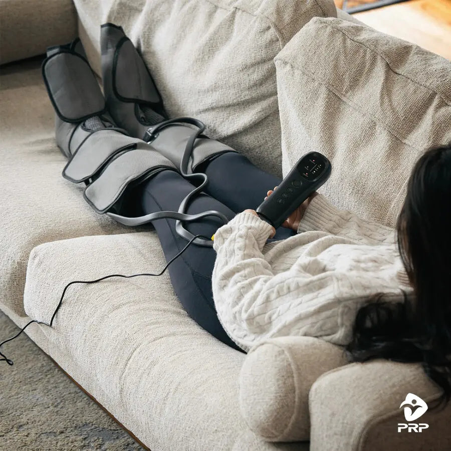 Lifestyle image of PRP® LegTech compression boots in use, woman lying on couch holding controller while massaging legs.