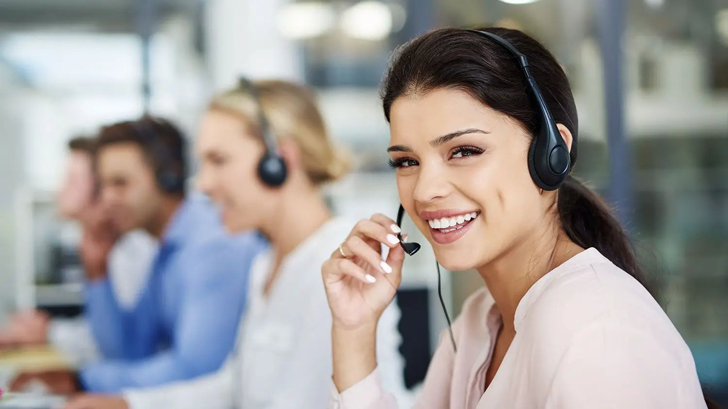 A smiling PRP customer service agent wearing a headset in a busy call center environment.