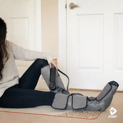 PRP® LegTech leg massager in use, user sitting on floor adjusting wrap with handheld controller for foot and calf massage.